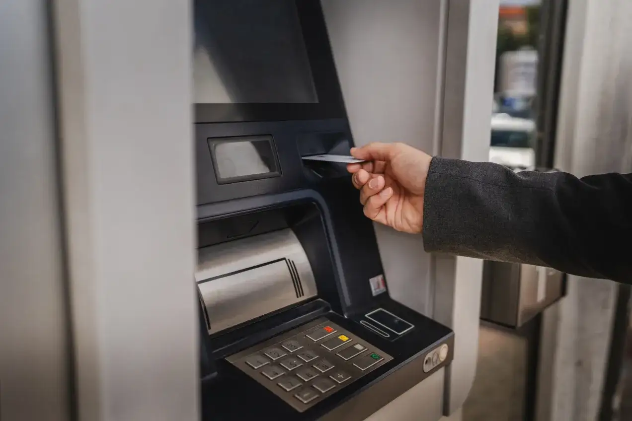 Dłoń wsuwa kartę do bankomatu, by sprawdzić, ile można wypłacić.