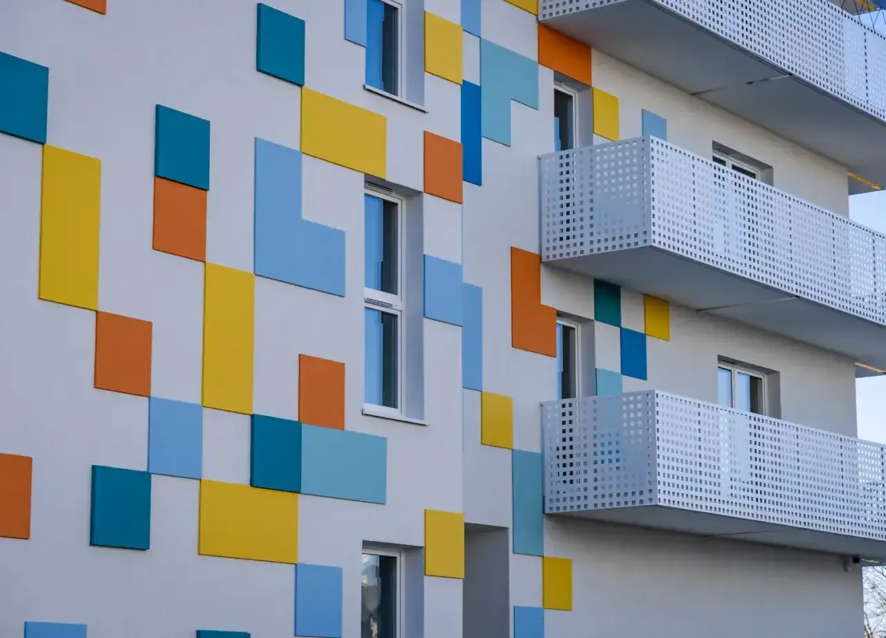 Nowoczesny budynek z kolorowymi, geometrycznymi panelami i białymi balkonami.
