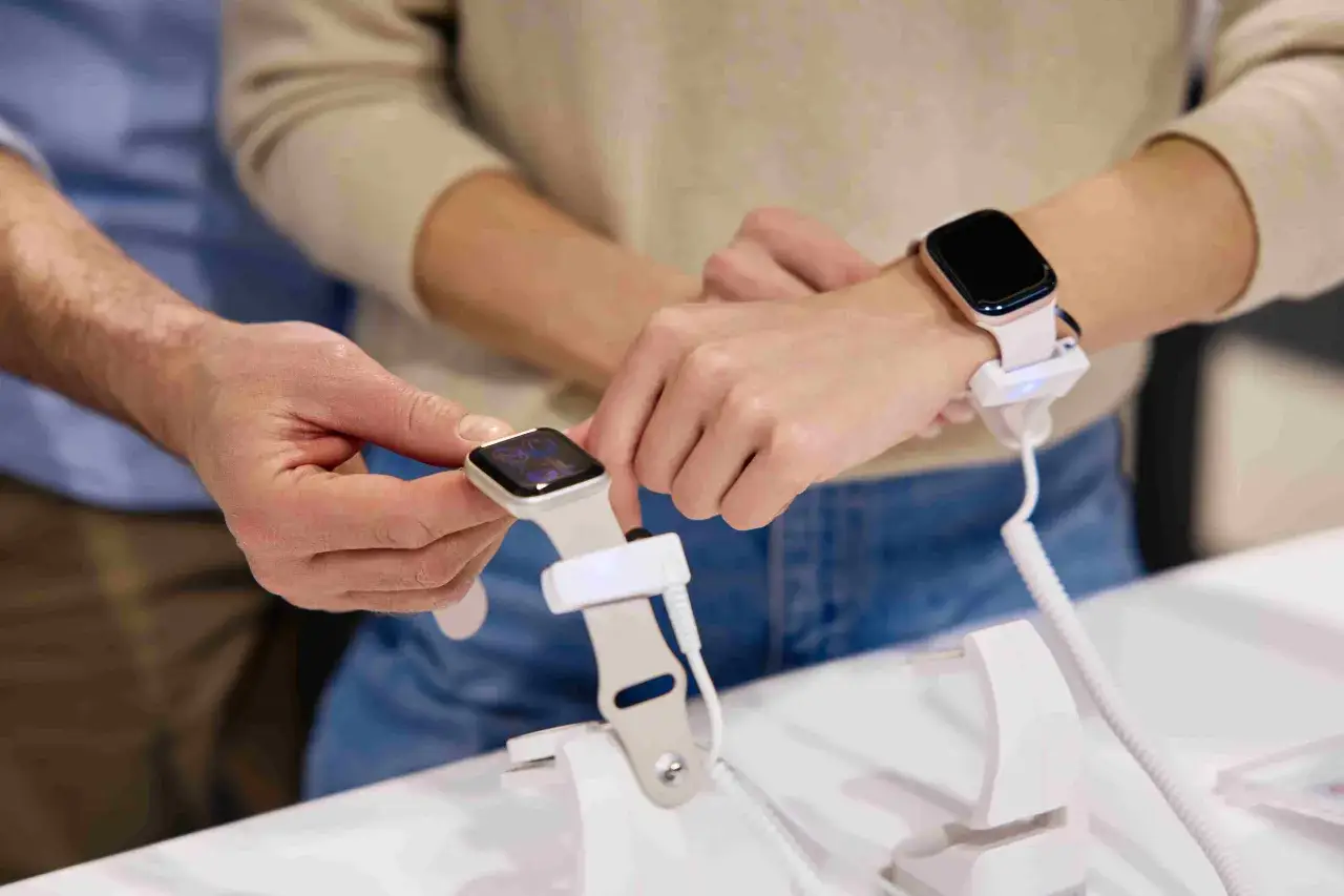 Un homme montre comment charger une montre connectée à une femme. La montre est fixée à un support de démonstration.