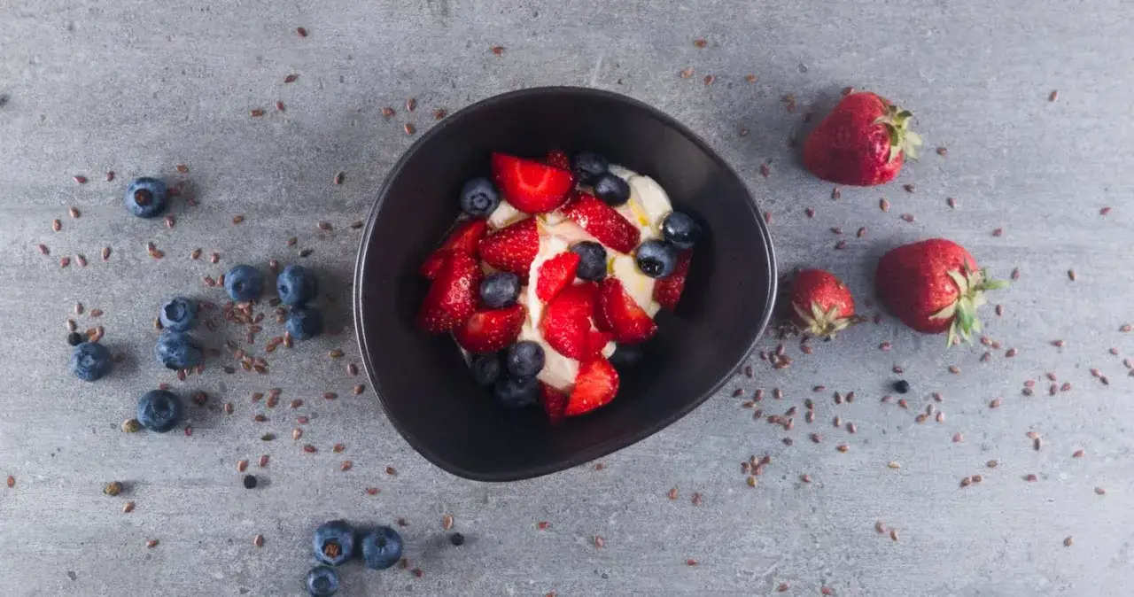 Schüssel mit cremigem low carb Joghurt, garniert mit frischen Erdbeeren und Blaubeeren. Leinsamen verstreut.