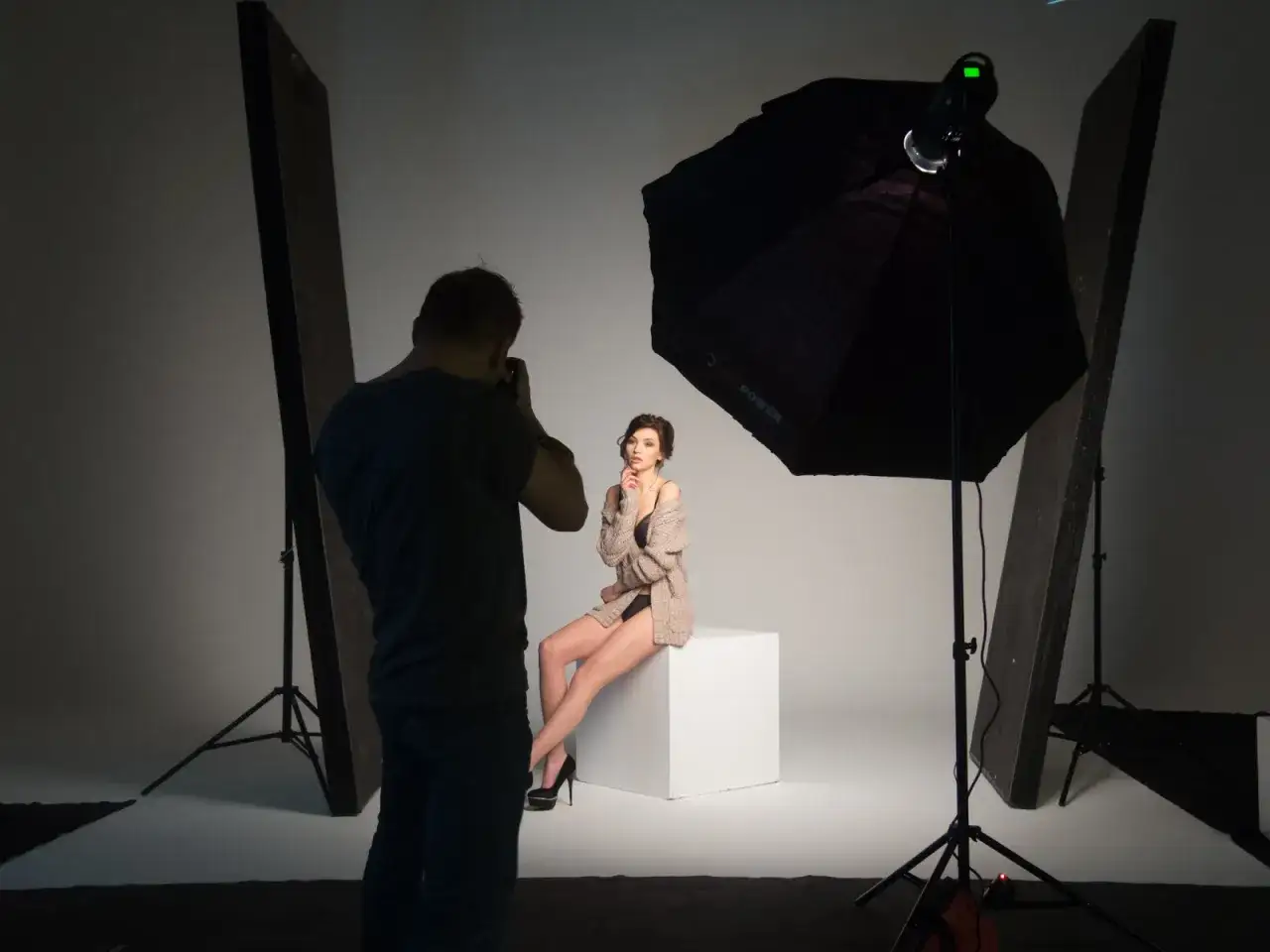 Fotograf ustawia lampy w studio, by oświetlić modelkę siedzącą na kostce.