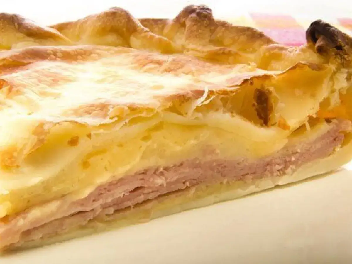 Rebanada de tarta de jamón y queso, con capas de masa dorada, jamón rosado y relleno cremoso. ¡Un bocado delicioso!
