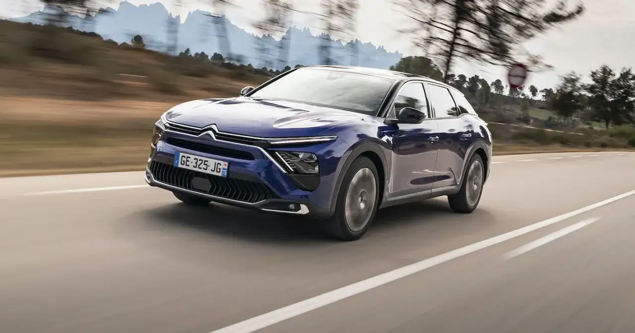 Granatowy Citroën C5 X, nowoczesny mpv, pędzi po krętej drodze wśród wzgórz.