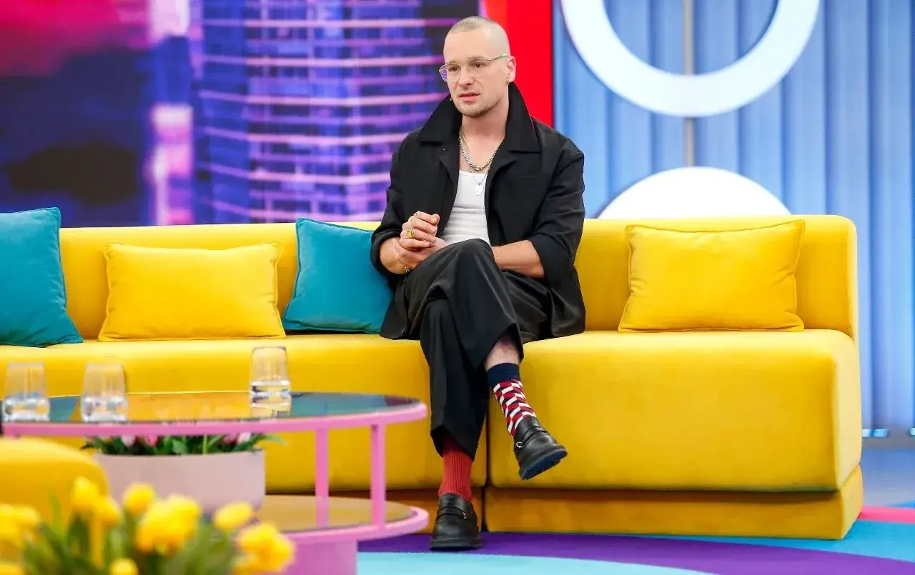Krzysztof Zalewski w czarnym garniturze siedzi na żółtej kanapie, jakby przygotowywał się do nagrania jednego z jego filmów.