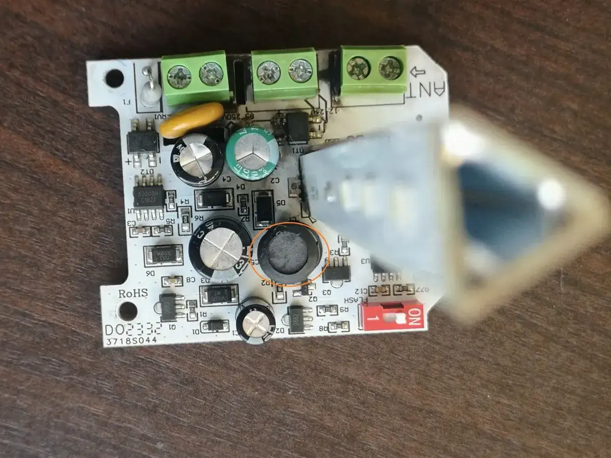Uszkodzona lampa ostrzegawcza bramy. Widoczny element elektroniczny z okrągłym, czarnym uszkodzeniem.