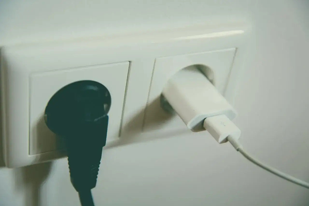 Czarna wtyczka i biała ładowarka w gniazdku elektrycznym. Bezpieczne uziemienie dla urządzeń.
