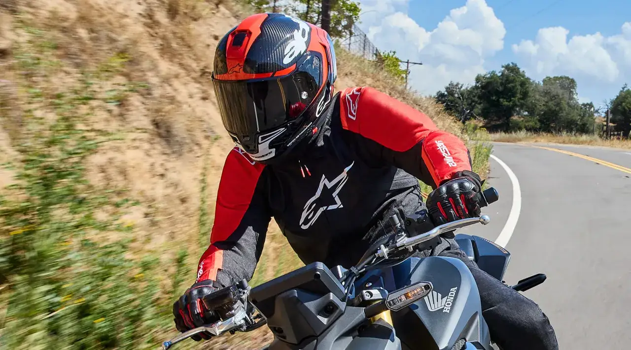 Motocyklista w czerwono-czarnym kasku i kurtce jedzie po krętej drodze.