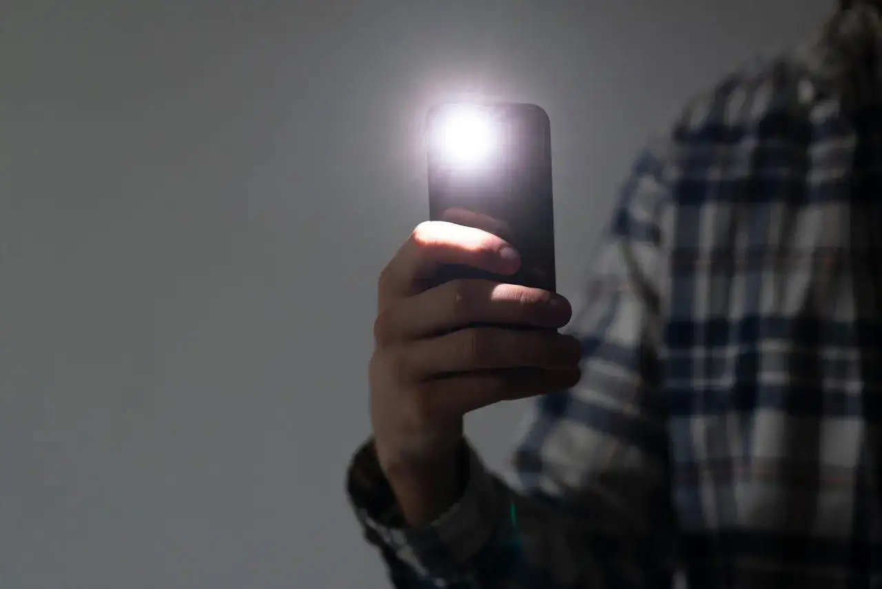 Dłoń trzyma smartfon z włączoną latarką.