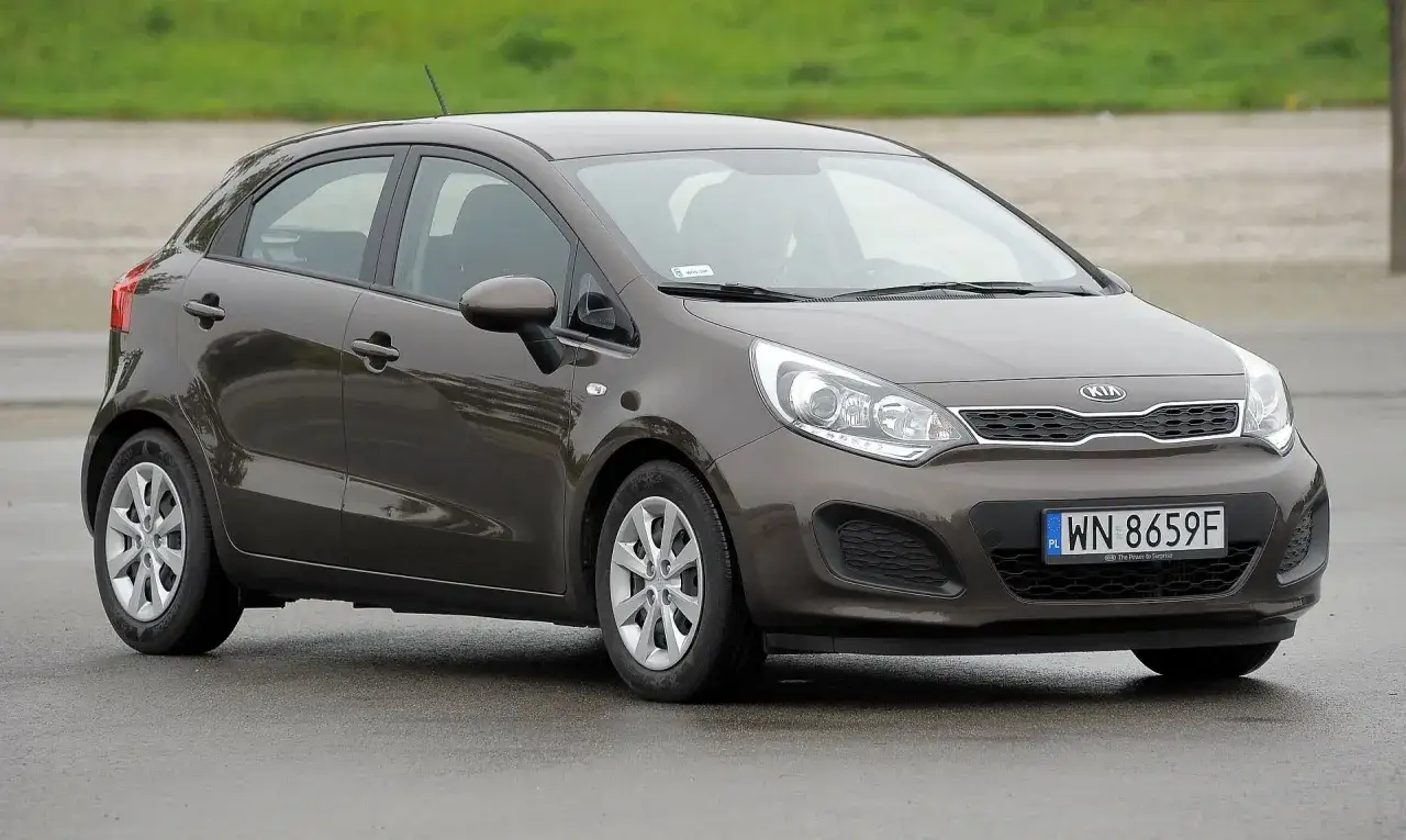 Brązowe kia rio 3 na mokrej nawierzchni, z widocznym numerem rejestracyjnym WN 8659F.