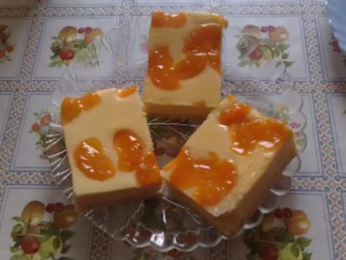 Drei Stücke faule weiber kuchen mit Mandarinen auf einem Tisch mit Blumenmuster.