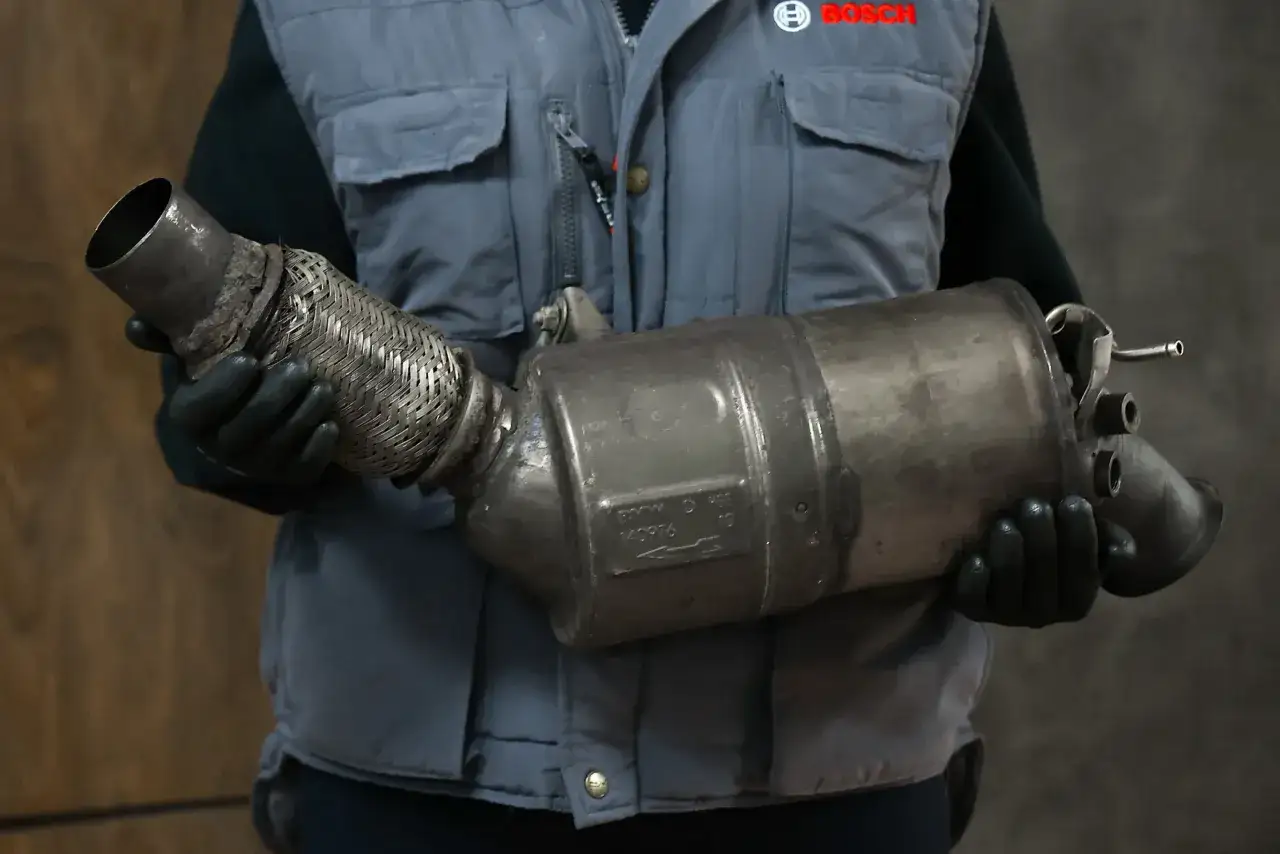 Mechanik w rękawiczkach trzyma zużyty element układu wydechowego, prawdopodobnie po problemach z wypalaniem DPF.