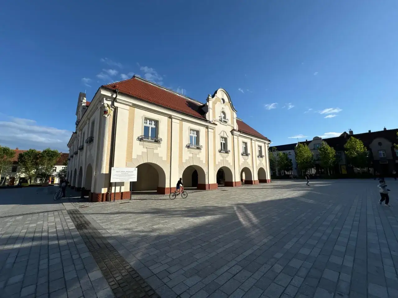 Ratusz w Jarocinie, plac z rowerzystą i dziećmi. Wiele się dzieje, to świetne jarocińskie wydarzenia!