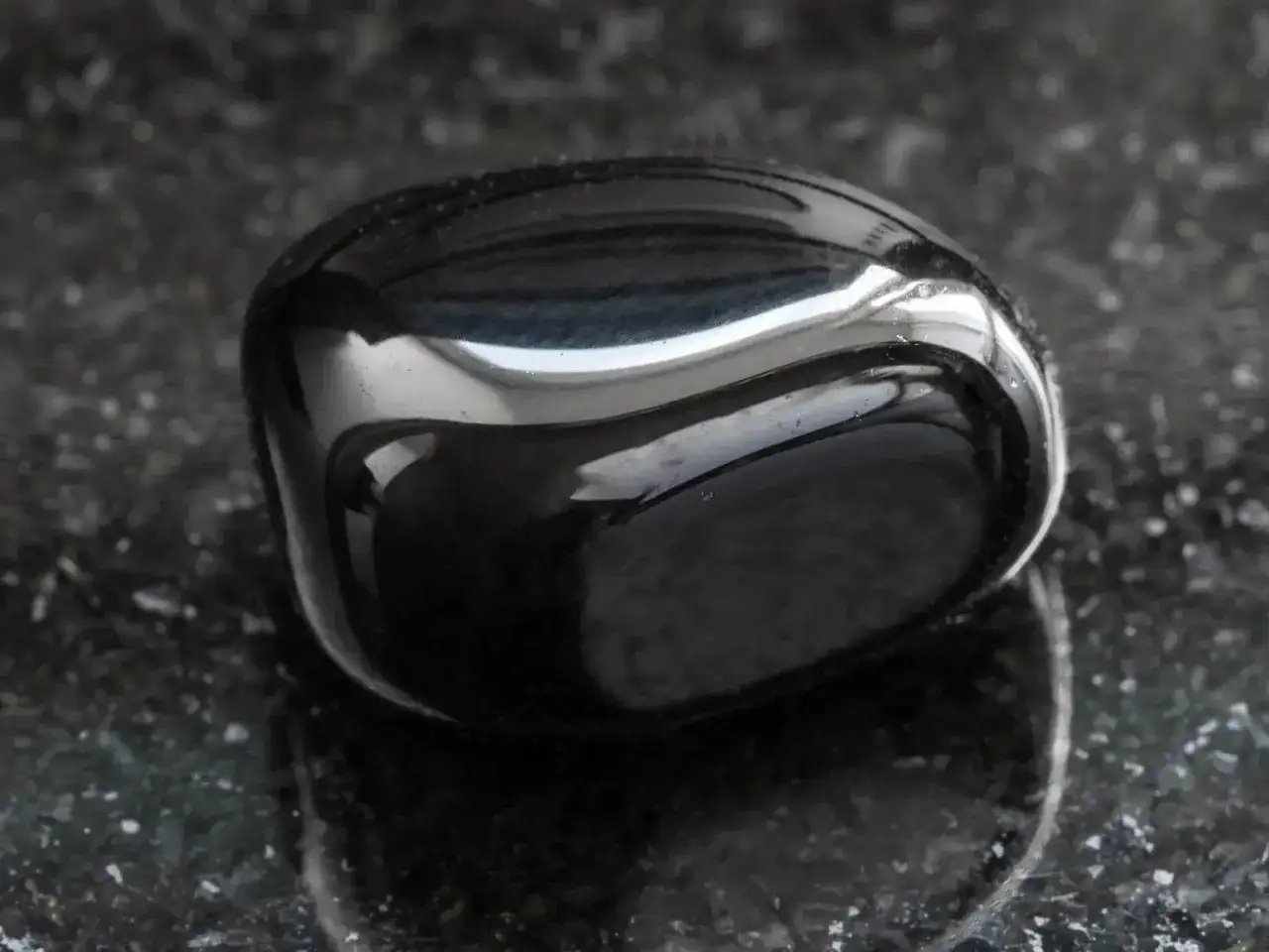 Glatter, glänzender onyx stein liegt auf einer dunklen, gesprenkelten Oberfläche.