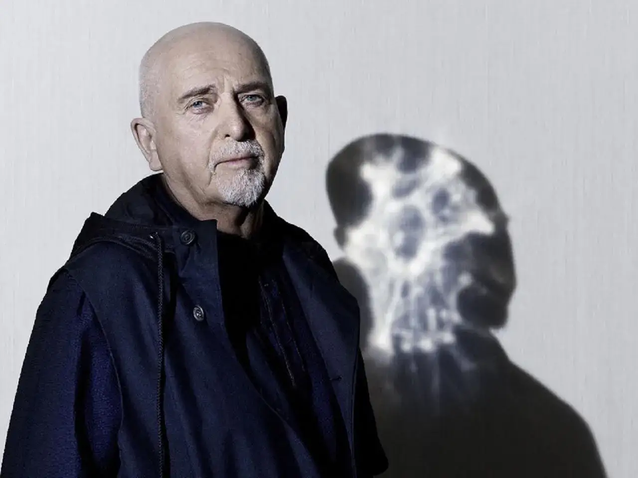 Peter Gabriel z charakterystycznym cieniem na ścianie, zapowiadający nową płytę.