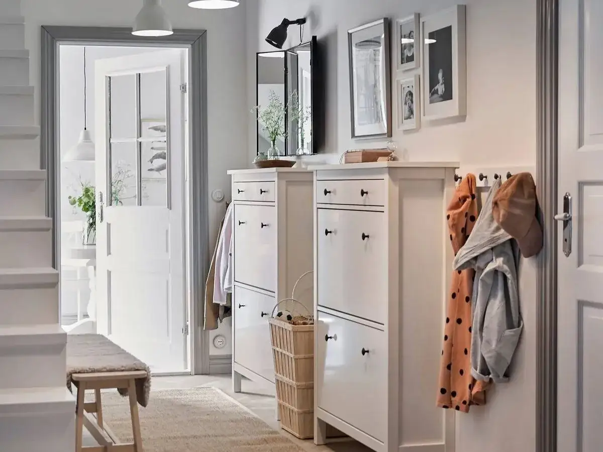 Elegante decoración de entradas y recibidores: zapateros blancos, perchero con abrigos y un banco de madera invitan a entrar.