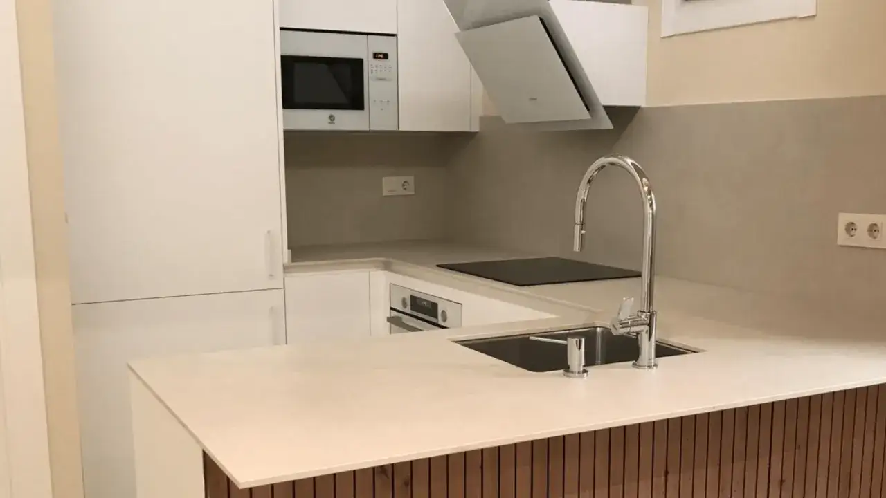 Cocinas pequeñas modernas con electrodomésticos integrados, encimera clara y grifería cromada.