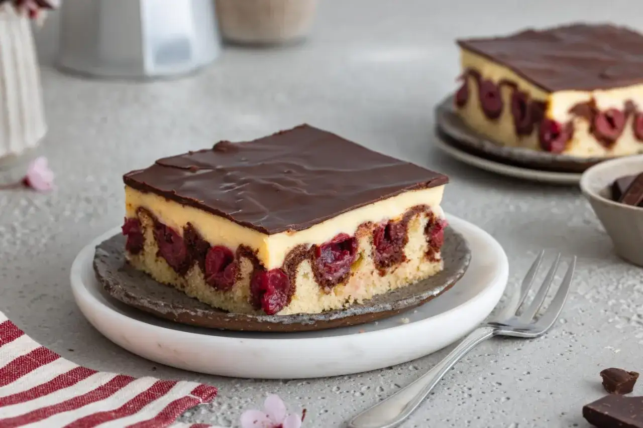 Ein Stück saftiger Kirsch-Schoko-Blechkuchen mit zarter Vanillecreme und Schokoladenglasur. Perfekt für leckere Blechkuchen Rezepte.