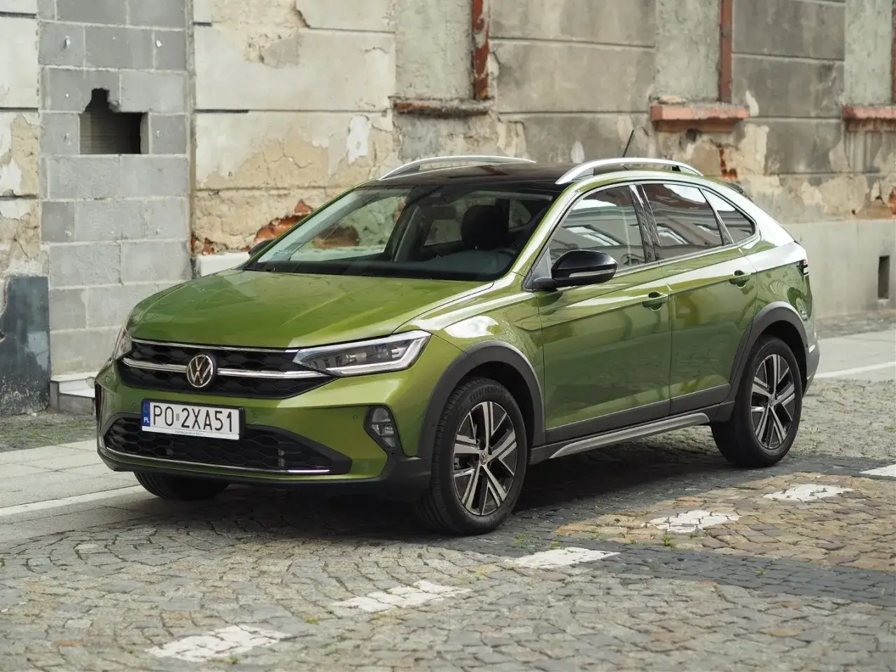 Zielony Volkswagen Taigo na brukowanej ulicy, z charakterystycznym dachem i felgami.