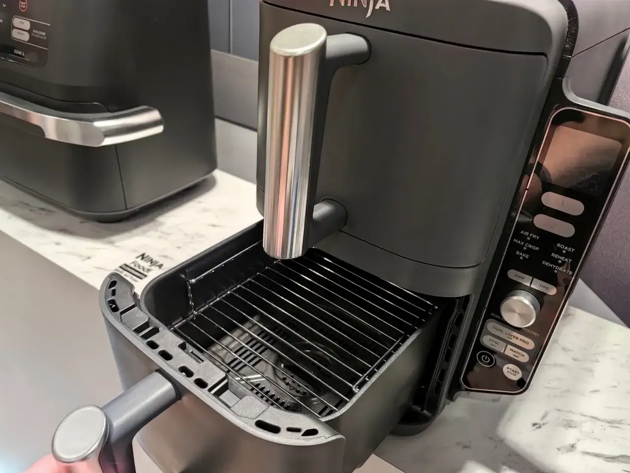 Nowoczesny czarny multicooker Ninja Foodi z wysuwanym rusztem. Ninja co to za firma? To producent innowacyjnych urządzeń kuchennych.