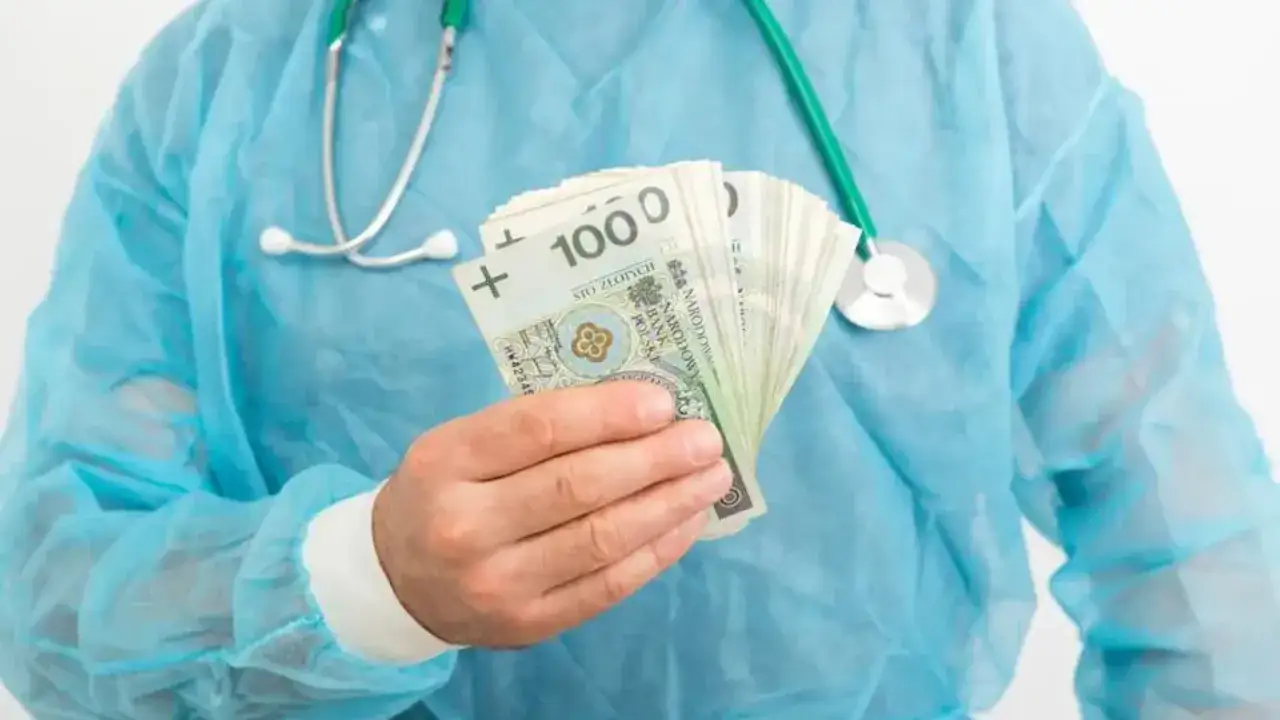 Lekarz rezydent w niebieskim fartuchu trzyma w dłoni plik banknotów 100 zł. Pytanie brzmi: ile zarabia lekarz rezydent?