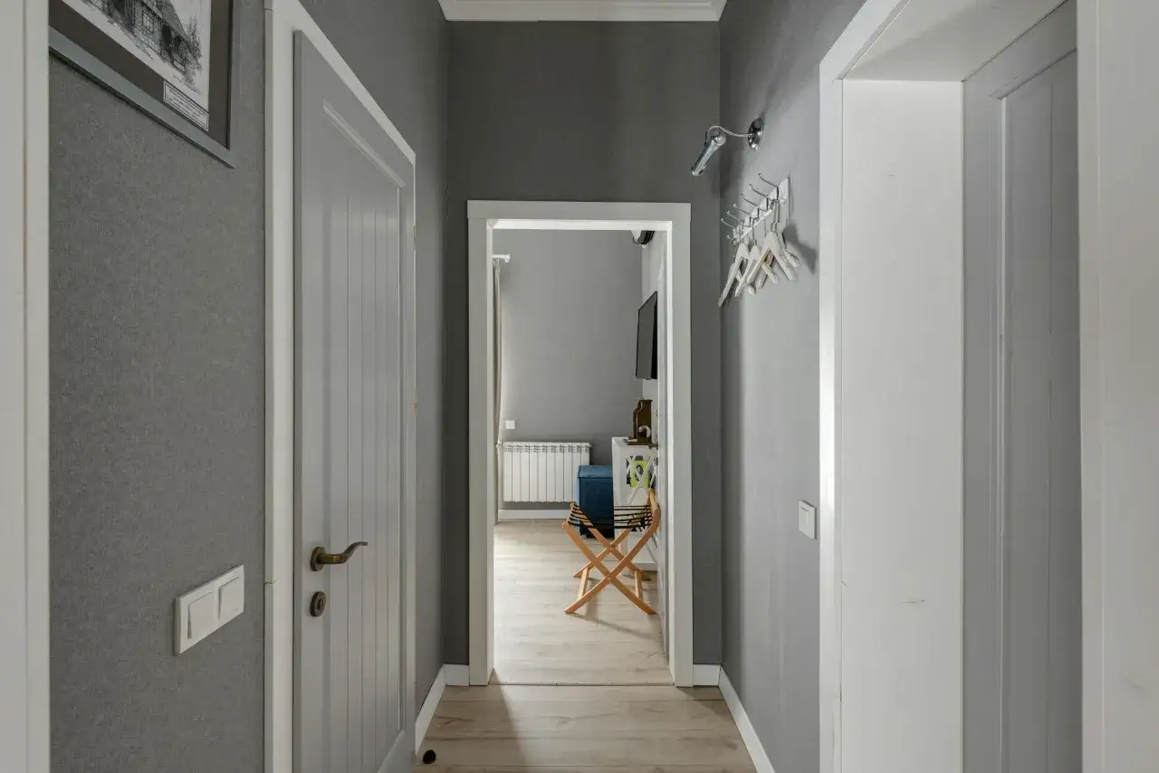 Pasillos con encanto, con paredes grises, puertas blancas y un cuadro en la pared. Se vislumbra una habitación con un radiador y un banco.