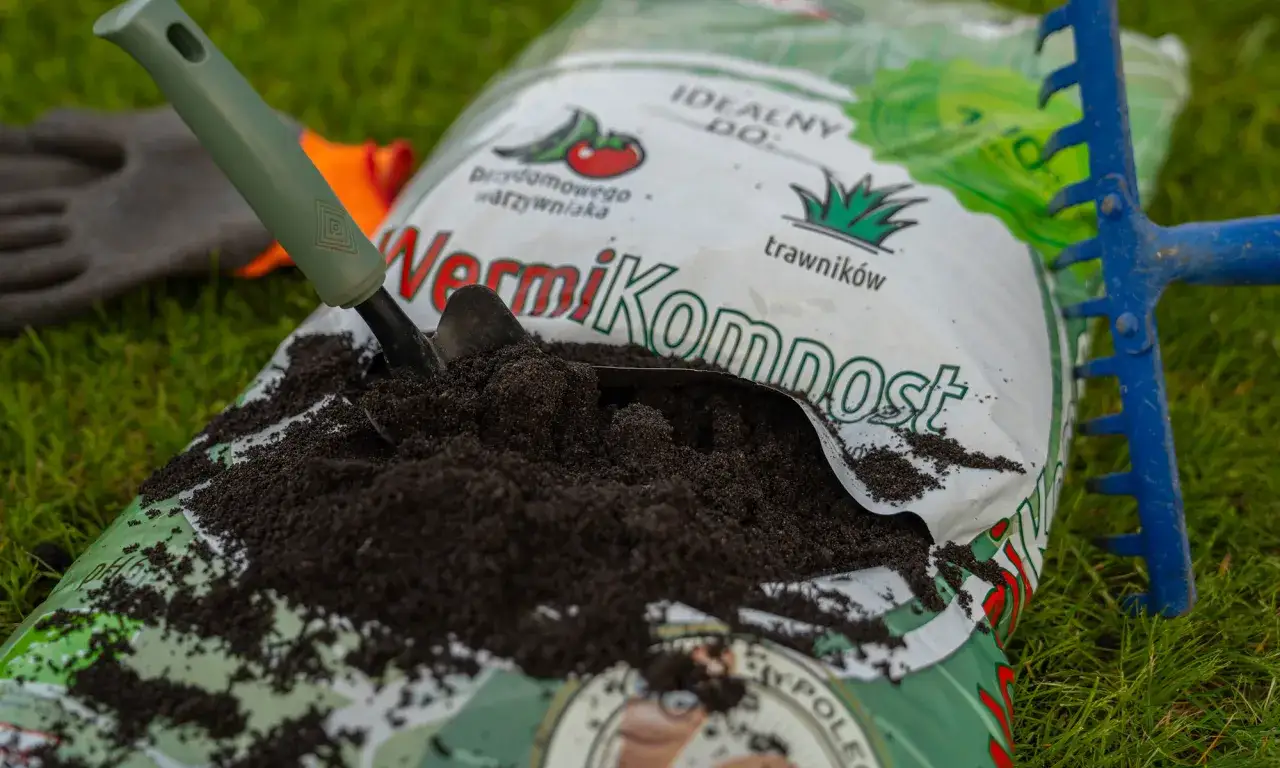 Worek z wermikompostem, łopatka i grabki na trawie. Idealny do warzywnika i trawników.