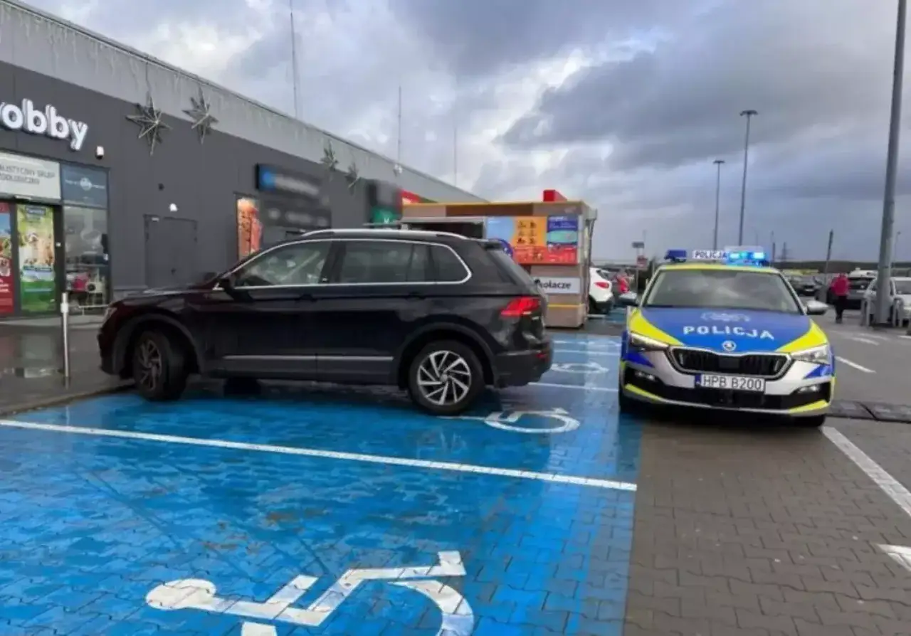 Czarny SUV zaparkowany na niebieskim miejscu dla niepełnosprawnych, obok radiowóz policyjny. To pytanie o to, jak długo można parkować na miejscu dla niepełnosprawnych, jest tu bardzo aktualne.