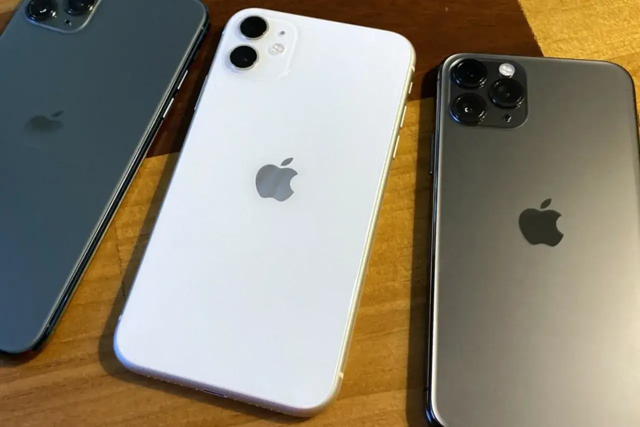 Trois iPhones 11, blanc et gris, sur un fond en bois. La date de sortie de l'iPhone 11 était le 20 septembre 2019.