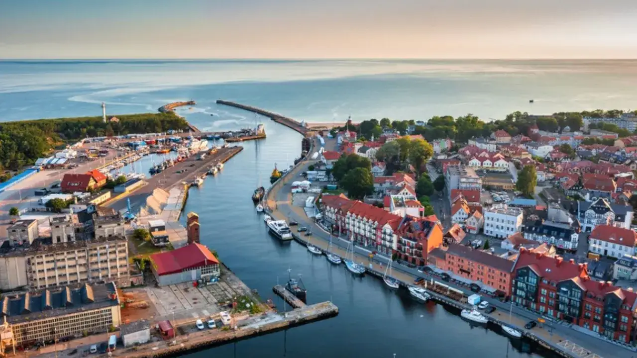 Widok z lotu ptaka na port i miasteczko, gdzie leży Ustka. Widać łodzie, budynki i morze.