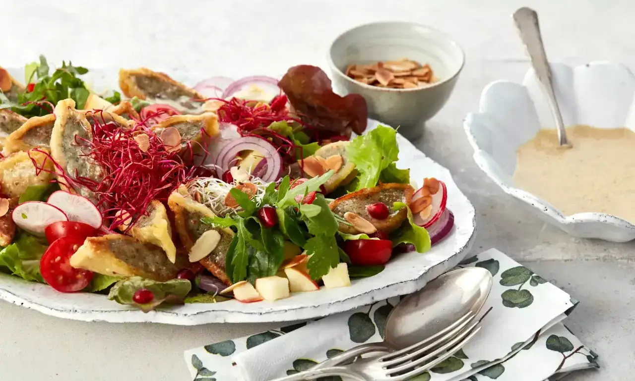 Herzhafter Maultaschen Salat mit knackigem Gemüse, roten Zwiebeln, Granatapfelkernen und Mandelsplittern. Dazu eine cremige Sauce.