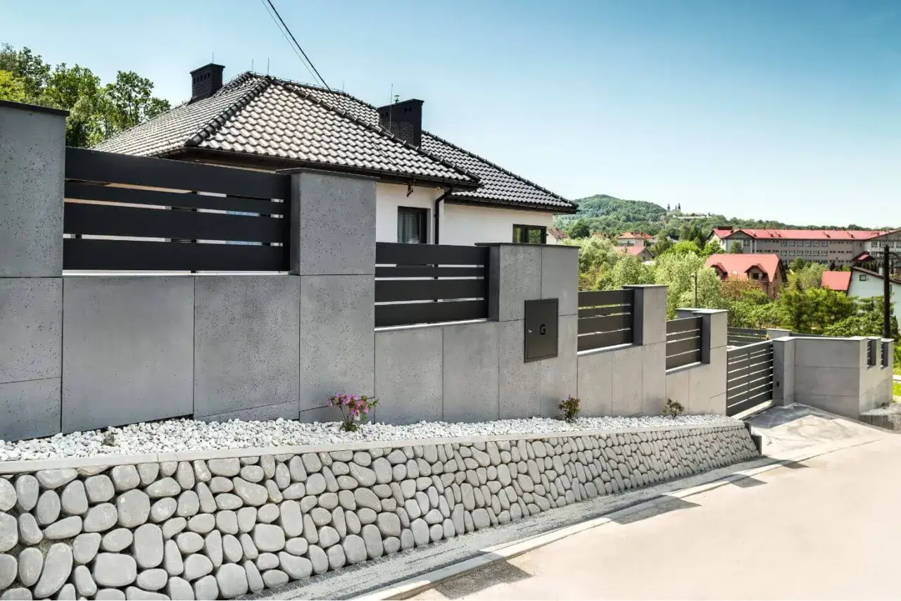 Nowoczesne ogrodzenie z betonu architektonicznego, z czarnymi elementami i kamiennym murkiem. Inspiracja, jak zrobić ogrodzenie z betonu architektonicznego.