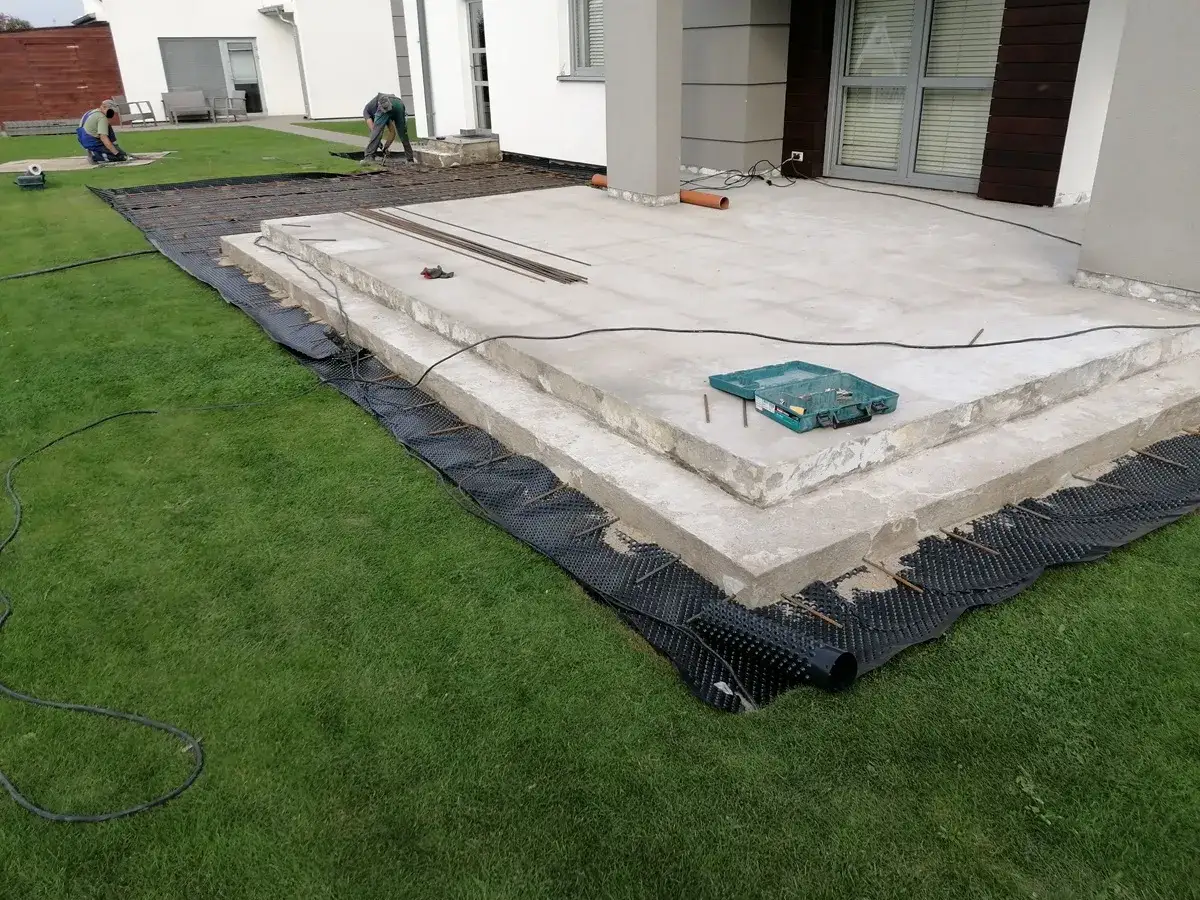 Budowa tarasu z betonu. Pracownicy przygotowują teren pod nową nawierzchnię, układając zbrojenie i materiały izolacyjne.
