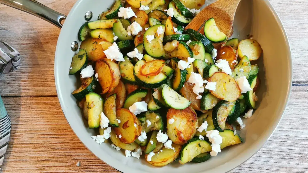 Herzhafte zucchini pfanne mit goldbraunen Kartoffelscheiben und zerbröseltem Feta, garniert mit frischen Kräutern.