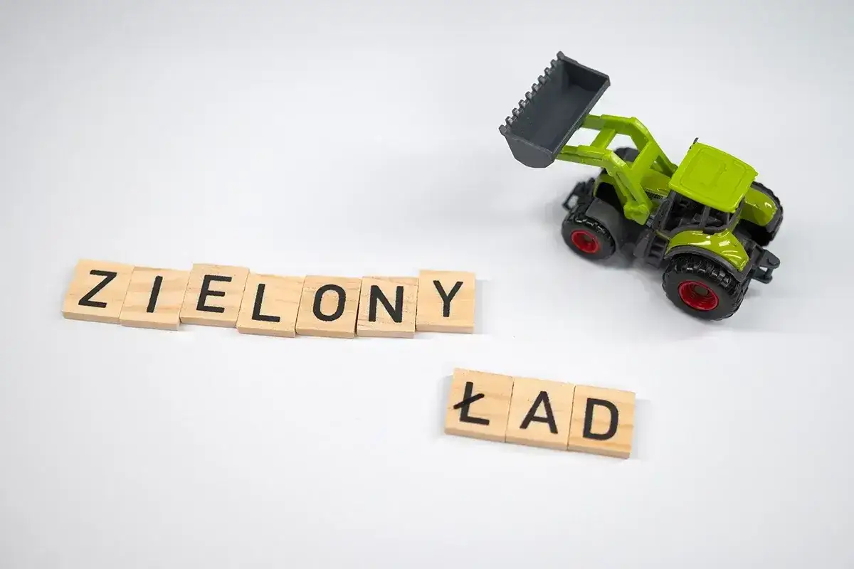 Drewniane klocki z literami "ZIELONY ŁAD" i zielona zabawka koparka na białym tle.