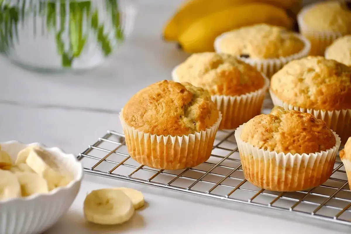 Frisch gebackene bananen muffins auf einem Gitter, daneben eine Schüssel mit Bananenscheiben.