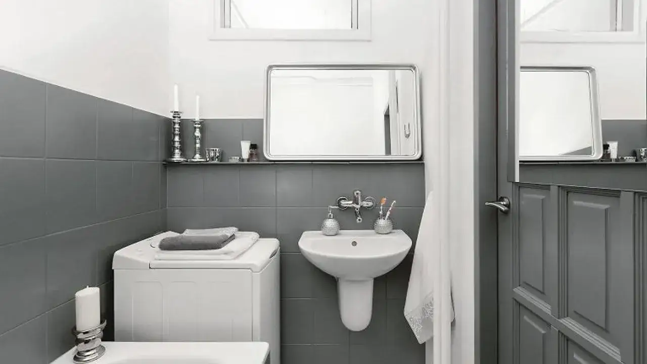 Baño moderno con azulejos grises, lavadora y lavabo. Un ejemplo de reformas de baños antes y después, con un estilo minimalista y funcional.