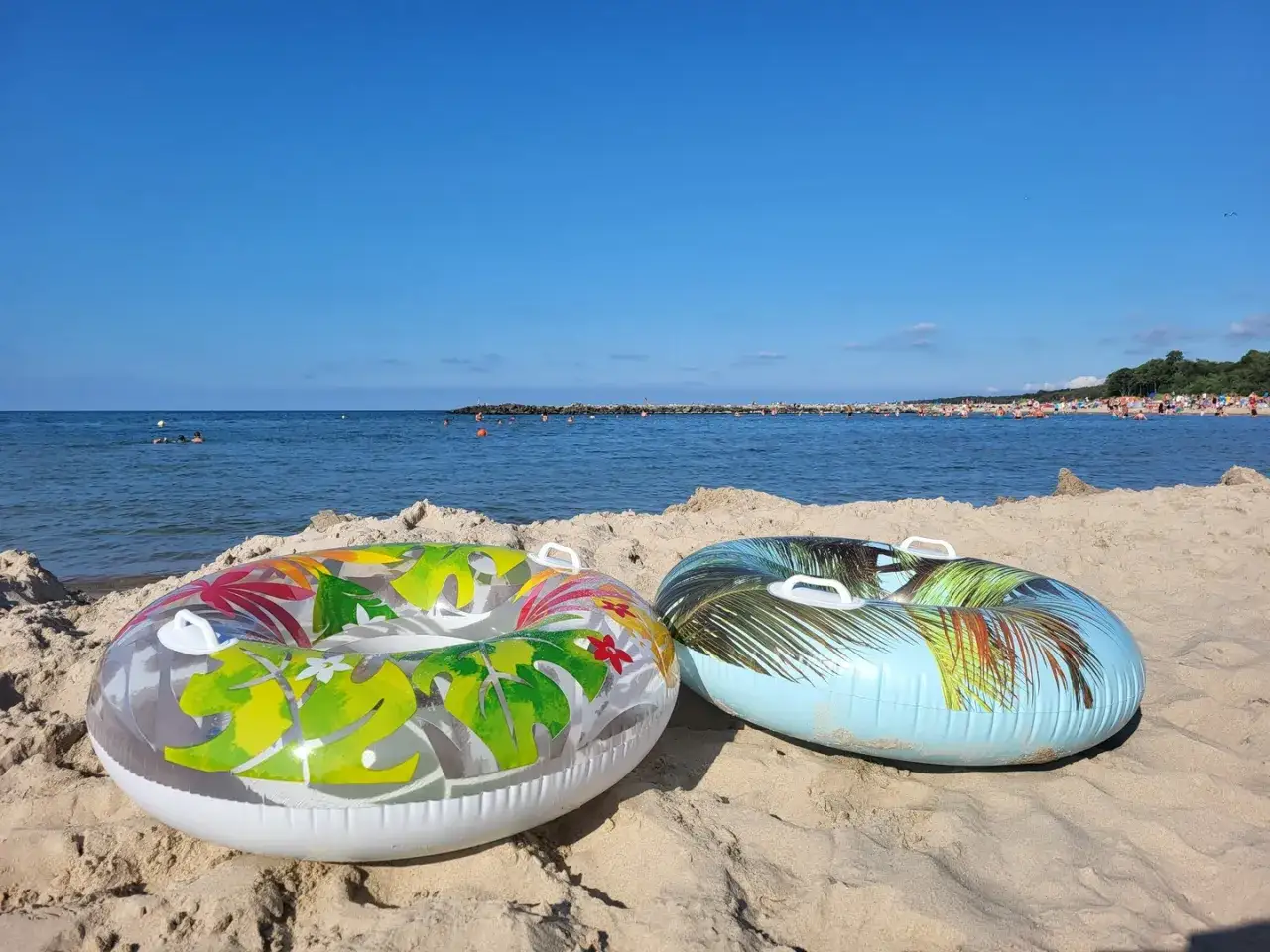 Dwa dmuchane koła na piaszczystej plaży, morze i tłumy ludzi w tle. Idealne na wakacje.pl opinie.