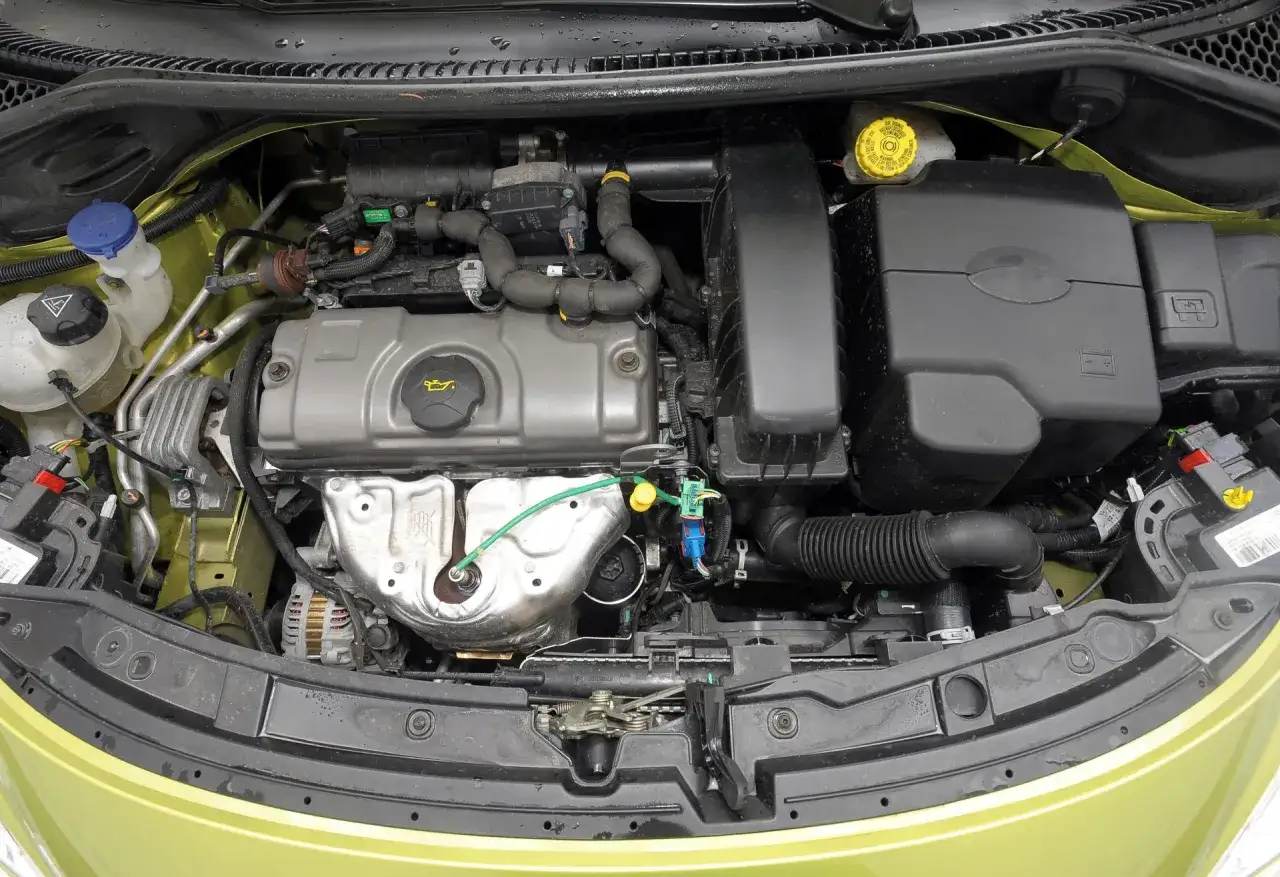 Silnik peugeot 207 1.4 benzyna. Widok komory silnika z widocznymi elementami, takimi jak alternator, obudowa filtra powietrza i zbiorniczek płynu chłodniczego.