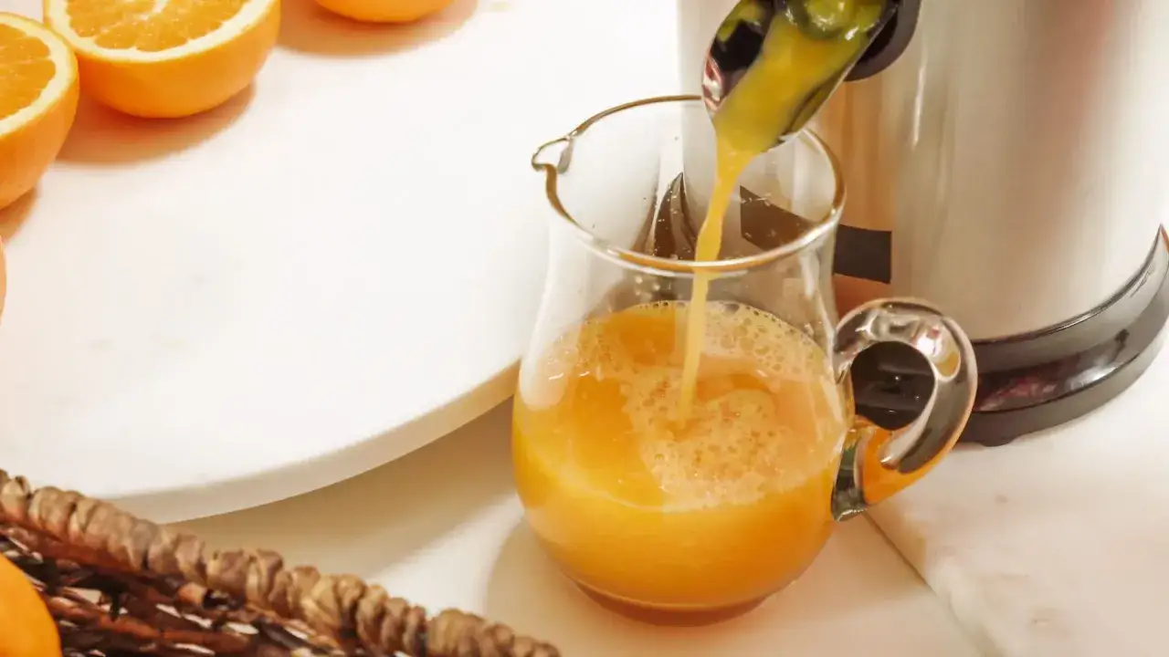 Frisch gepresster Orangensaft fließt in ein Glas. Orangen sind bereit, um zu zeigen, was man entsaften kann.