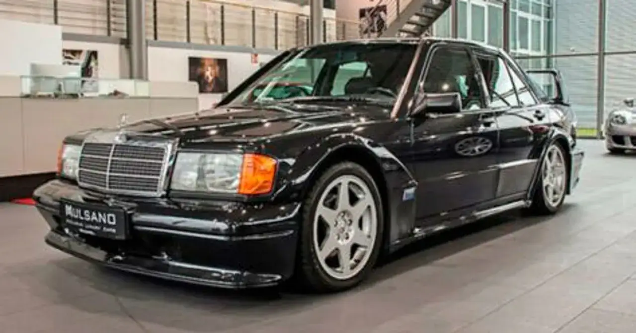 Czarny Mercedes 190 Evo z charakterystycznym spojlerem i felgami, stojący w salonie samochodowym.