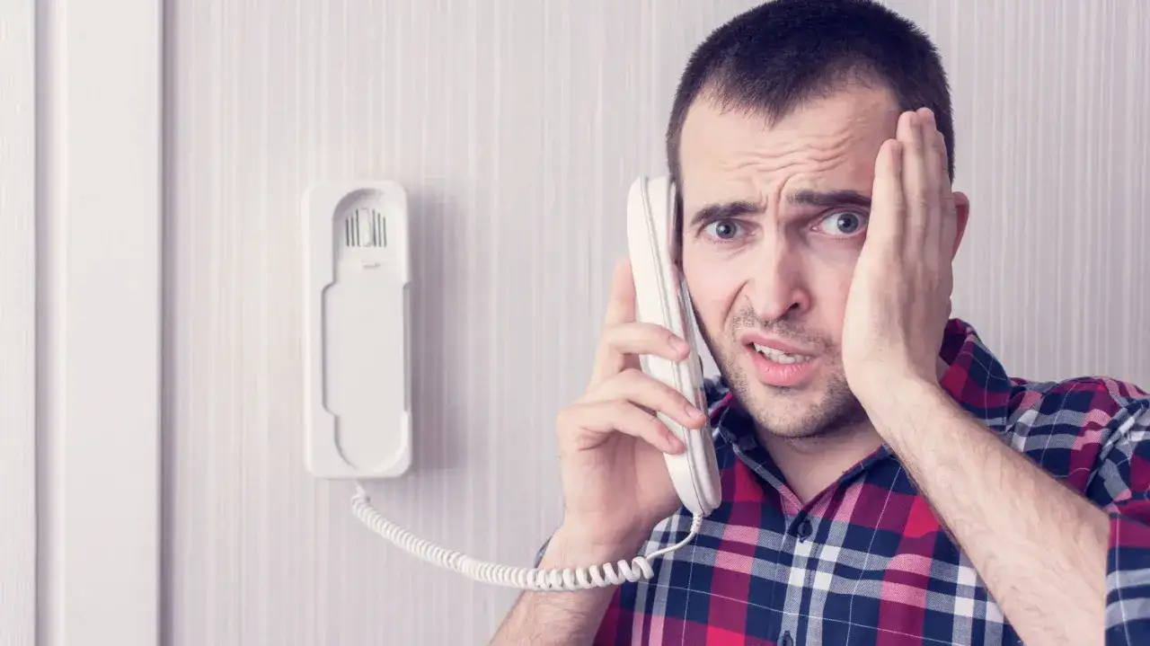 Zmartwiony mężczyzna dzwoni z telefonu domofonowego. Gdzie zgłosić niedziałający domofon?