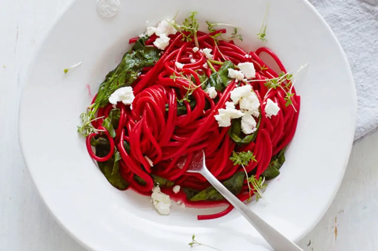 Rote-Bete-Spaghetti mit Spinat, Feta und Kresse auf einem Teller.