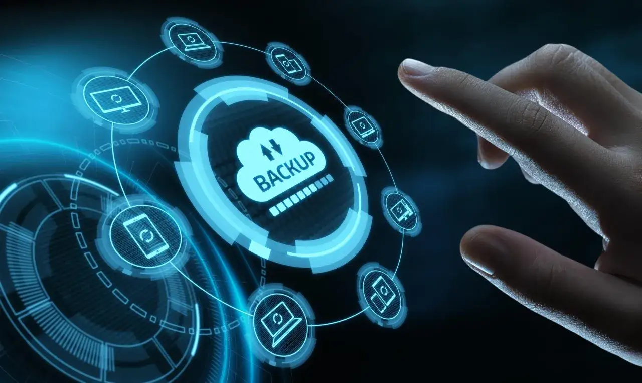 Palec dotyka interfejsu chmury z napisem "BACKUP". Ikony komputerów i smartfonów wskazują na kopia bezpieczeństwa danych.
