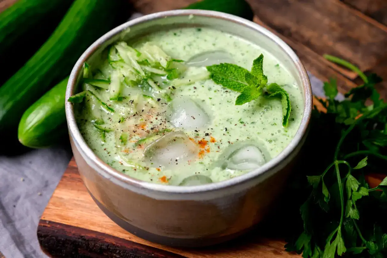Erfrischende cremige kalte Gurkensuppe mit Eiswürfeln, Minze und geriebenen Gurken, garniert mit Pfeffer und Paprikapulver.