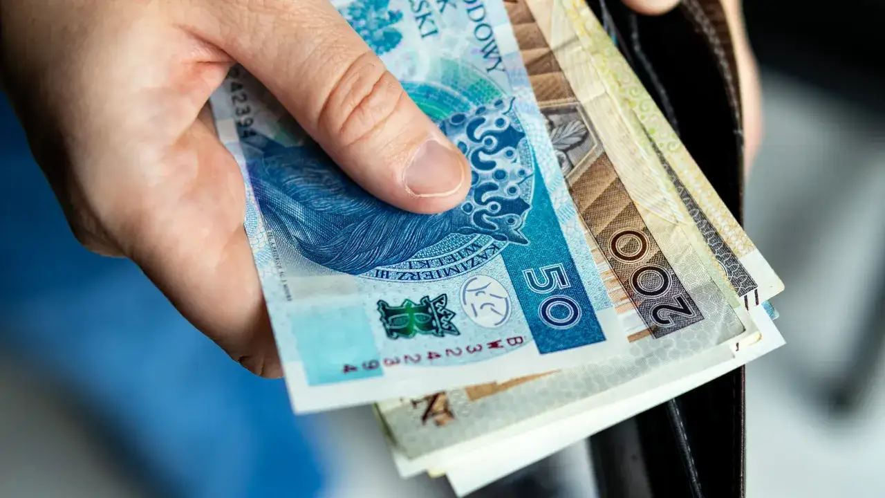 Dłoń trzyma polskie banknoty. Wkrótce jawność wynagrodzeń 2026, więc warto wiedzieć, ile zarabiamy.