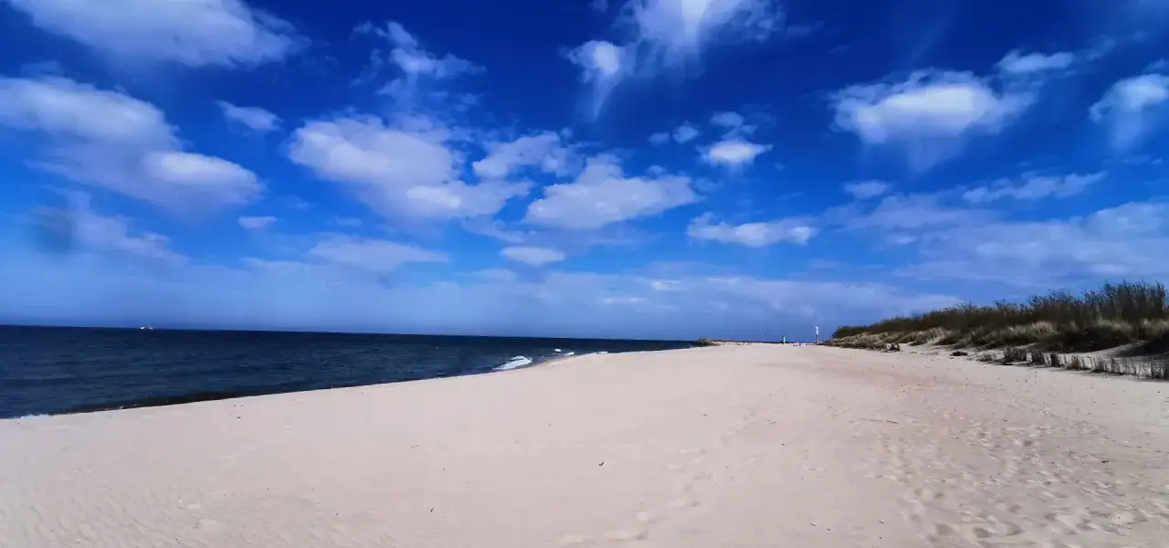 Piękna, słoneczna pogoda na sierpień nad morzem. Szeroka, piaszczysta plaża, spokojne morze i błękitne niebo z białymi chmurami.
