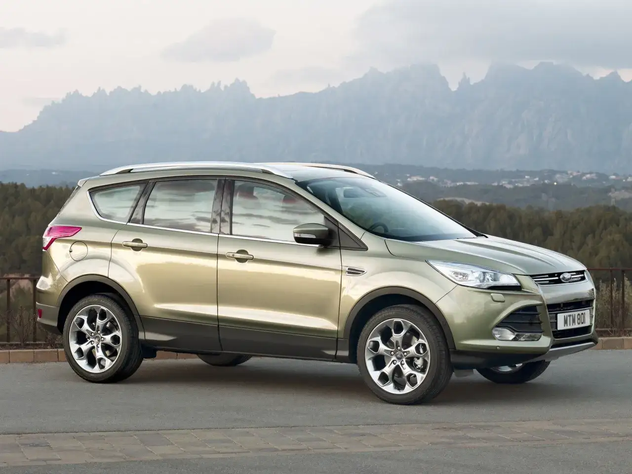 Złoty Ford Kuga na tle górskich krajobrazów. Wiele osób chwali ten model, a jego opinie są pozytywne.