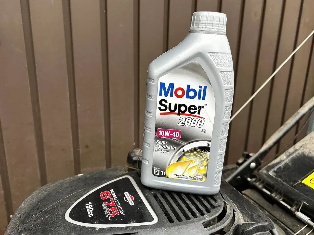 Butelka oleju Mobil Super 2000 10W-40 na silniku kosiarki Briggs & Stratton.