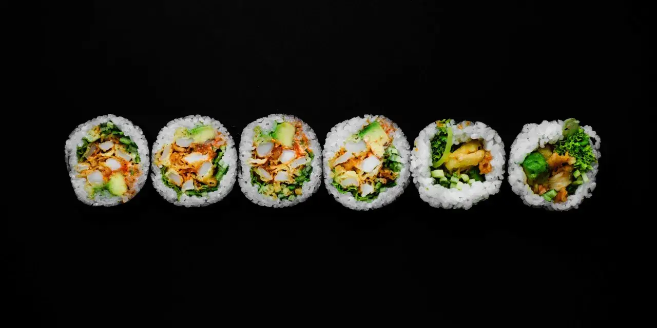 Sześć kawałków futomaki, czyli dużych rolek sushi, z ryżem, awokado, warzywami i smażonymi kawałkami.