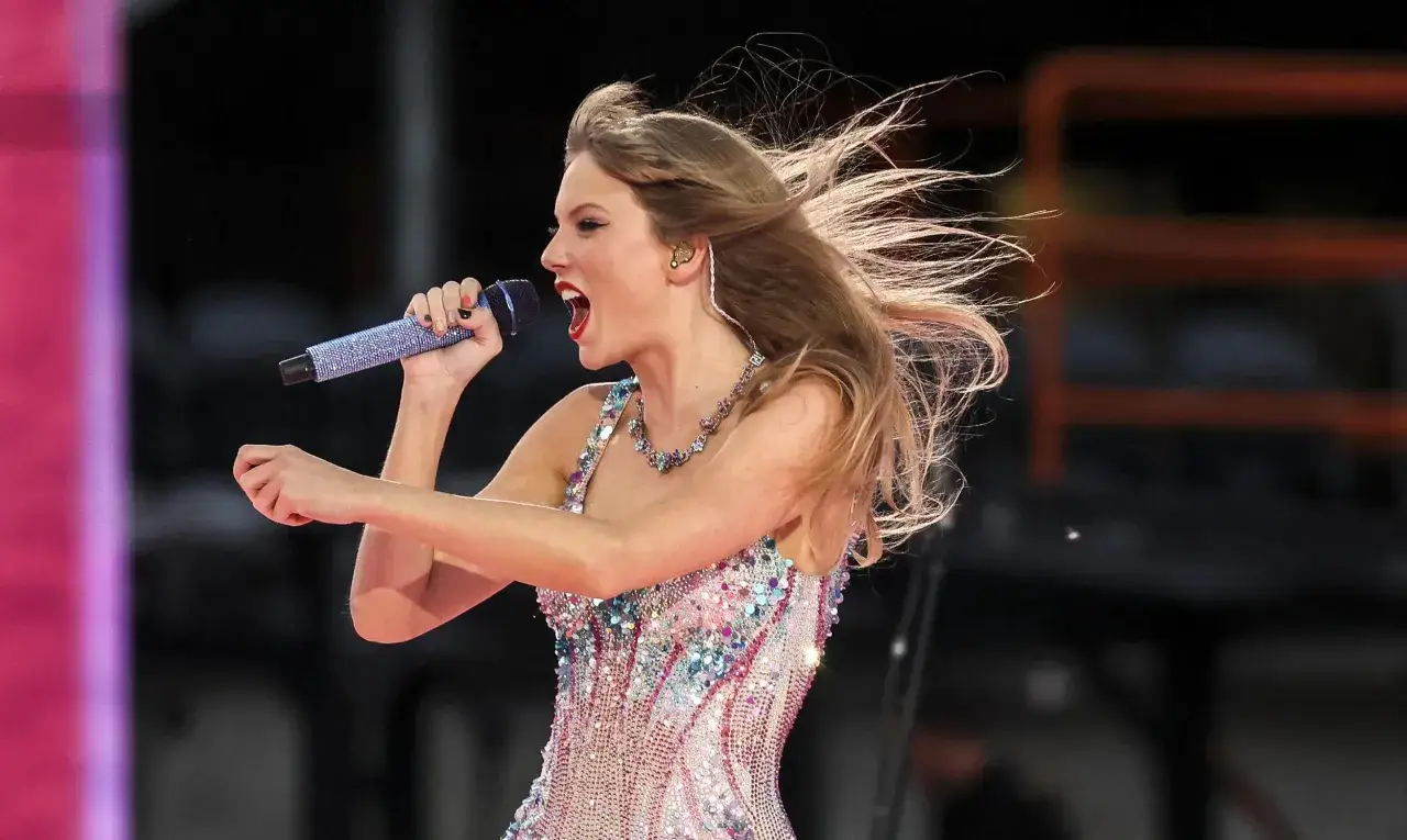 Taylor Swift w błyszczącej sukience śpiewa na koncercie w Warszawie, włosy rozwiane przez wiatr.